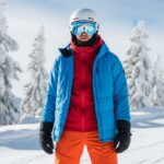 Narciarz w ubraniu zimowym stoi na śnieżnym stoku z sosnami i czystym niebem w tle