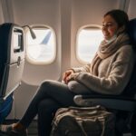 Młoda kobieta w samolocie z poduszką podróżną, ubrana w sweter, legginsy i z maseczką pod brodą